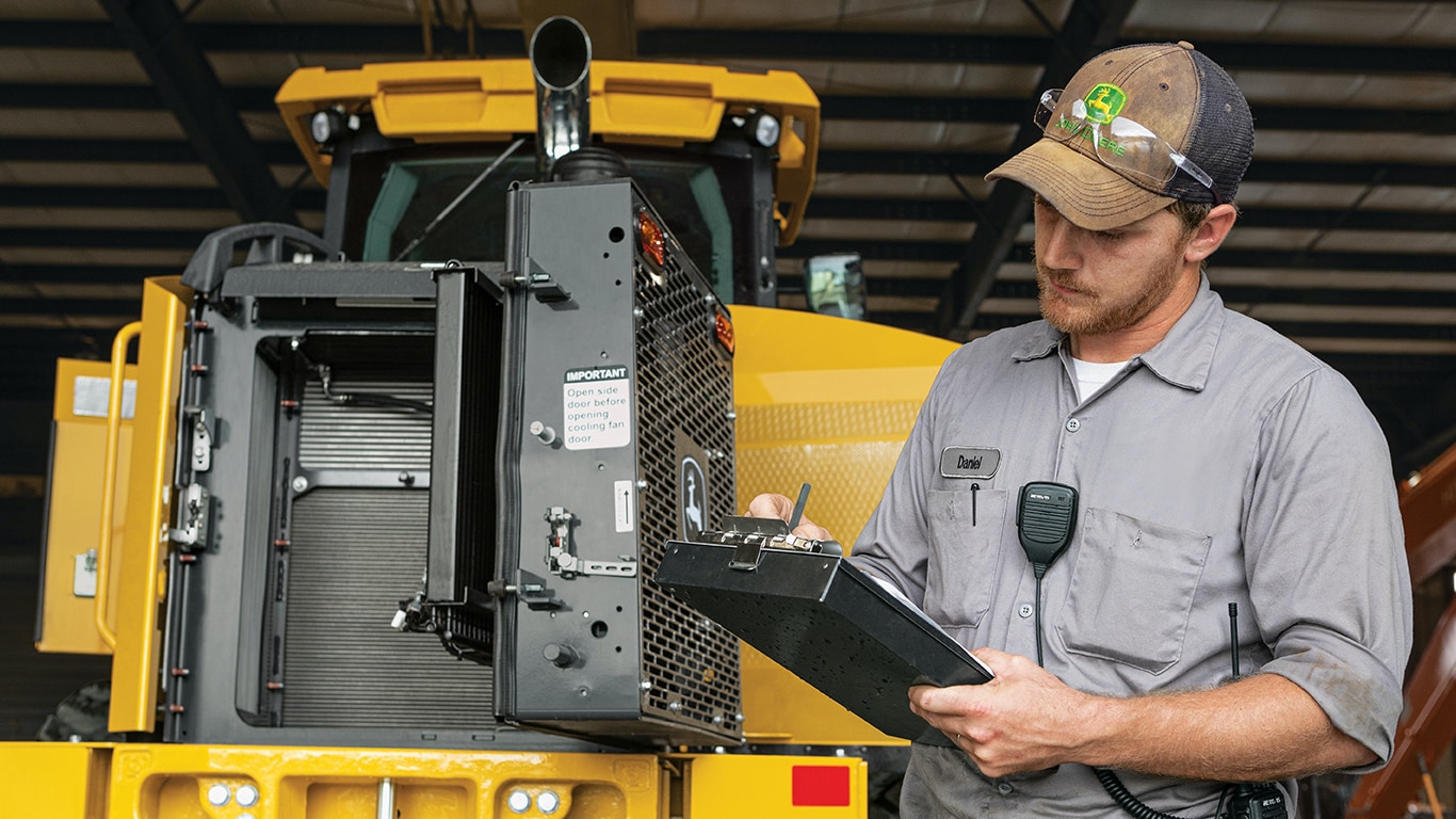 Image of a John Deere operator reviewing materials in front of construction equipment